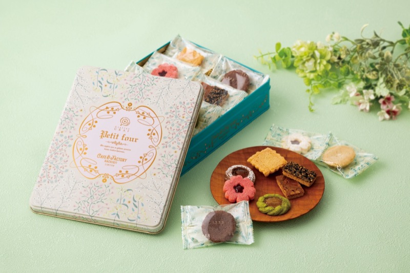 花柄の蓋にCAFE & FACTORY HACHIOJI LIMITEDと書かれた青い缶が開き、花型ジャムサンドや抹茶、チョコなど複数のクッキーが木皿と缶の中に並んでいる