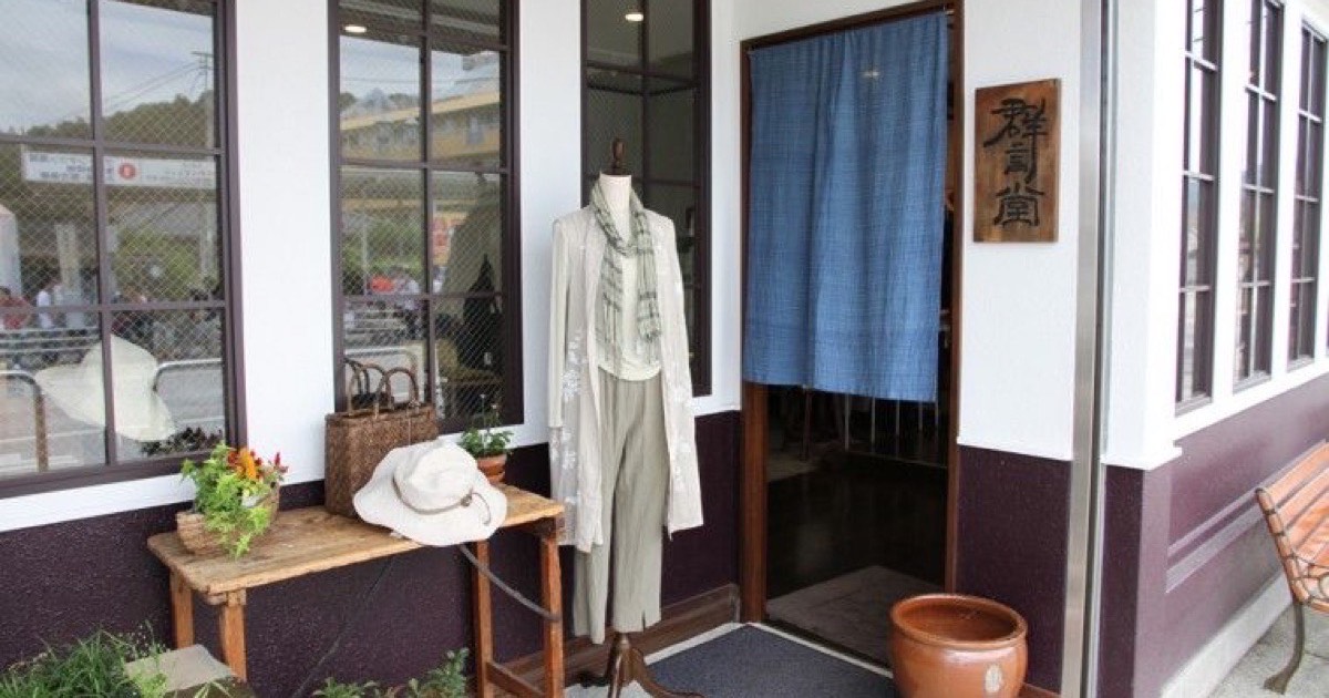 白い壁と群言堂の木札、藍色ののれんがあるJR高尾駅北口店の入口