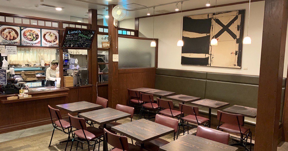 木のテーブルと緑のベンチが並ぶichigendoの店内。左にカレーなどのメニュー写真がある