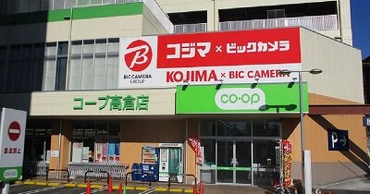 白い外壁の商業施設。1階左に緑地のコープ高倉店看板、中央に赤いコジマ×ビックカメラの大型看板、右のガラス扉上に緑のco-opロゴ