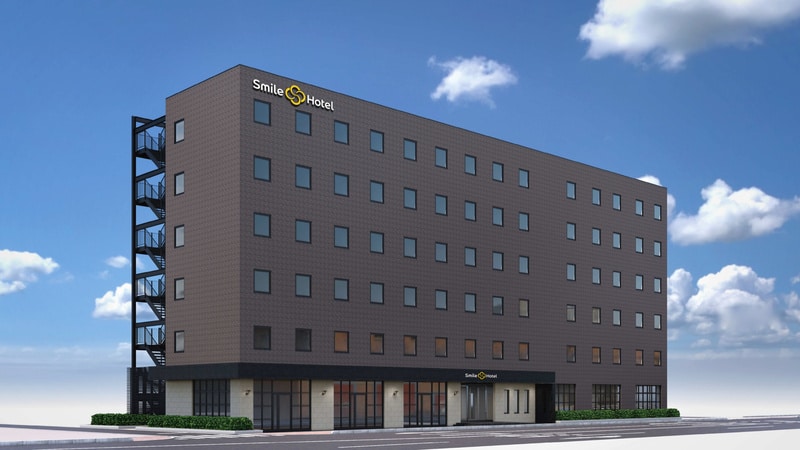 青空の下に立つダークグレーの7階建てホテル外観パース。屋上にSmile Hotelの白い文字と黄色いマーク、1階入口のひさしにも同ロゴ、左側に黒い非常階段がある