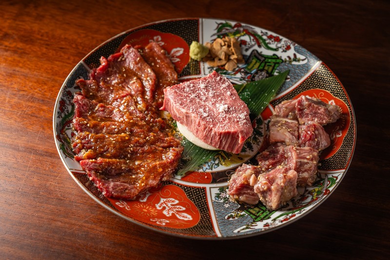 色絵の丸皿にタレの薄切り肉、塩を振ったヒレのブロック、サイコロ状の和牛。わさびとしょうがが添えられている