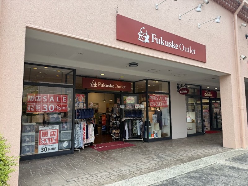 薄いピンクの壁に赤いFukuske Outlet看板がある店頭。ガラス面に閉店SALE 30%OFFの掲示があり、店内に靴下や衣類のハンガーが見える