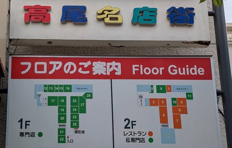 高尾名店街と書かれた看板の下にフロアのご案内。1階は専門店、2階はレストランと専門店の区画番号が色分けされている