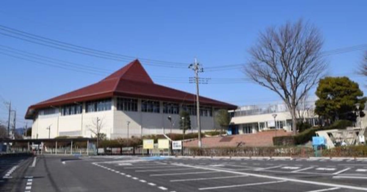 青空の下、赤い三角屋根の富士森体育館。手前は駐車場