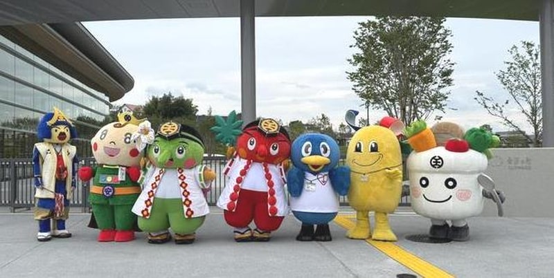桑都の杜の建物前に並ぶ八王子市のPRキャラクター7体の着ぐるみ。武者姿や赤と緑の天狗、青い鳥、黄色いキャラクター、白い丼のキャラクターなどが横一列に立っている