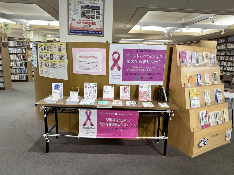 図書館内の展示台。ピンクのリボンの横断幕とパネル、乳がん検診を勧める本が並び、奥に書架が見える