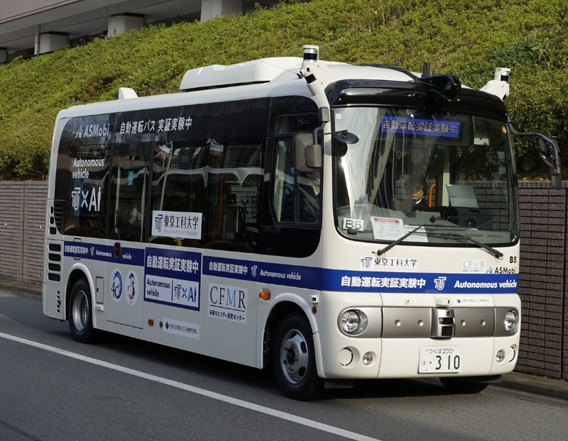 車体に「自動運転バス 実証実験中」「東京工科大学」「Autonomous vehicle」と表示され、屋根にセンサーを搭載した白い小型バスが道路脇に停車している