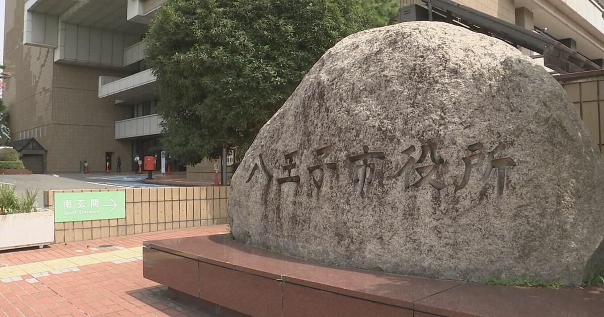 八王子市役所と刻まれた石。奥に市役所の建物と木がある
