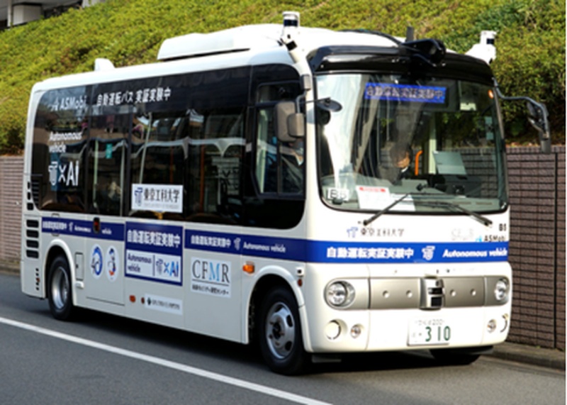車体に「自動運転バス 実証実験中」と表示し、行先表示器に「自動運転実証実験中」と出した白と紺色の小型バスが道路を走行している