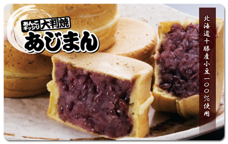 皿の上に大判焼のあじまんが重ねて置かれ、手前に半分に割ったあじまんの断面から粒あんがぎっしり詰まっている様子が見える写真。左上に「あんこギッシリ 大判焼 あじまん」のロゴ、右側に縦書きで「北海道十勝産小豆100%使用」と書かれている