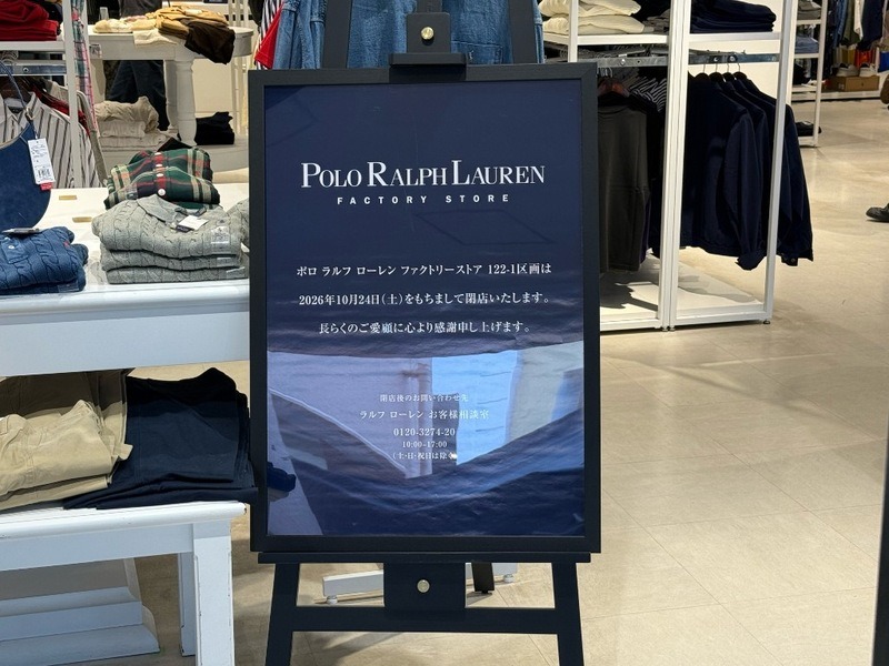 ポロ ラルフ ローレン ファクトリーストアの店内に置かれたネイビーの立て看板。POLO RALPH LAUREN FACTORY STOREのロゴの下に、2026年10月24日(土)をもちまして閉店いたしますという文言がある。左側の平台にはニットやシャツがたたんで並んでいる