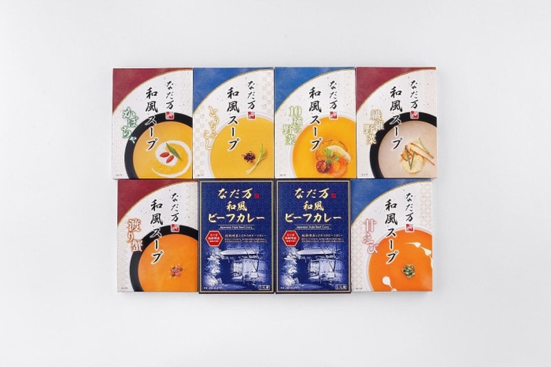 なだ万の箱入りレトルト商品8箱が2段に並ぶ。上段はかぼちゃ、とうもろこし、10種の野菜、繊維野菜の和風スープ、下段は渡り蟹の和風スープ、紺色の和風ビーフカレー2箱、甘えびの和風スープ