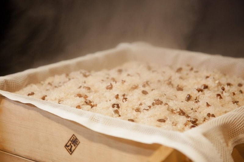 白い布を敷いた木のセイロに、湯気が立つお赤飯がふっくらと蒸し上がっている。木枠の手前に米八の焼き印がある