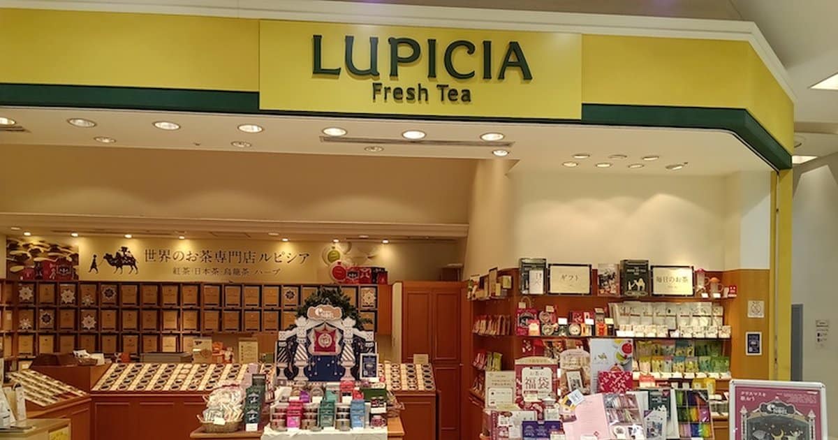 黄色い看板にLUPICIA FreshTEAと書かれた八王子オクトーレ1階のルピシア店舗。店内奥の壁一面に茶色い茶葉の箱が並び、手前の木目のカウンターに缶やギフトが置かれている