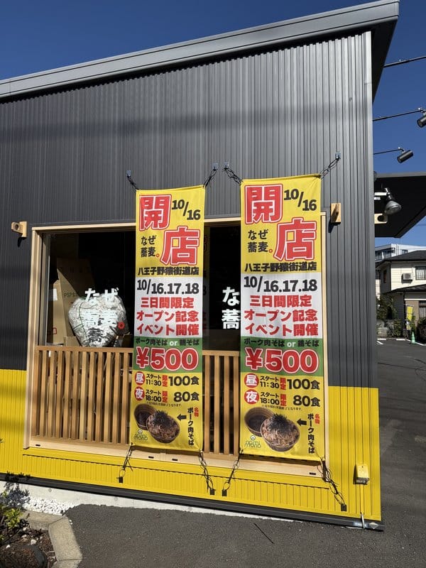 黒い壁と黄色い腰壁の窓の前に、10月16日開店と10月16日から18日の3日間限定でポーク肉そばまたは鶏そばが500円と書いた黄色いのぼりが2本並んでいる