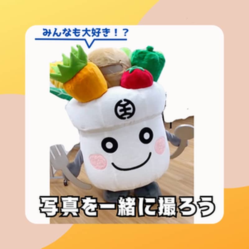 白い飯ごう型の着ぐるみはっちくん。頭にニンジンやピーマン、手にフォークを持ち、吹き出しにみんなも大好き!?、下に写真を一緒に撮ろううと書かれている