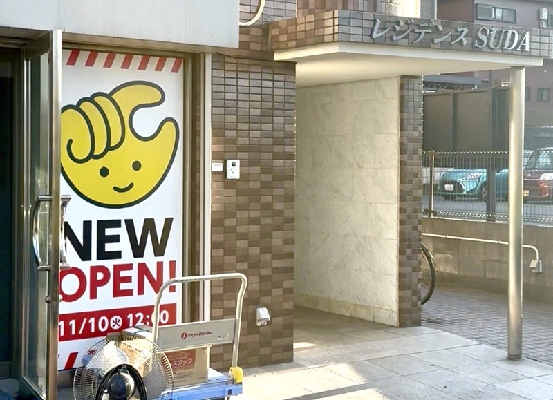 八王子市松木のマンション「レジデンスSUDA」1階入口。黄色い手のキャラクターとNEW OPEN!、11/10(火)12:00と書かれたチョコザップの開店告知がガラス扉に貼られ、右手のひさしにレジデンスSUDAの文字がある