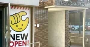 八王子市松木のレジデンスSUDA1階入口。黄色い手のキャラクターとNEW OPEN!のチョコザップ開店告知が貼られ、右手のひさしにレジデンスSUDAの文字がある