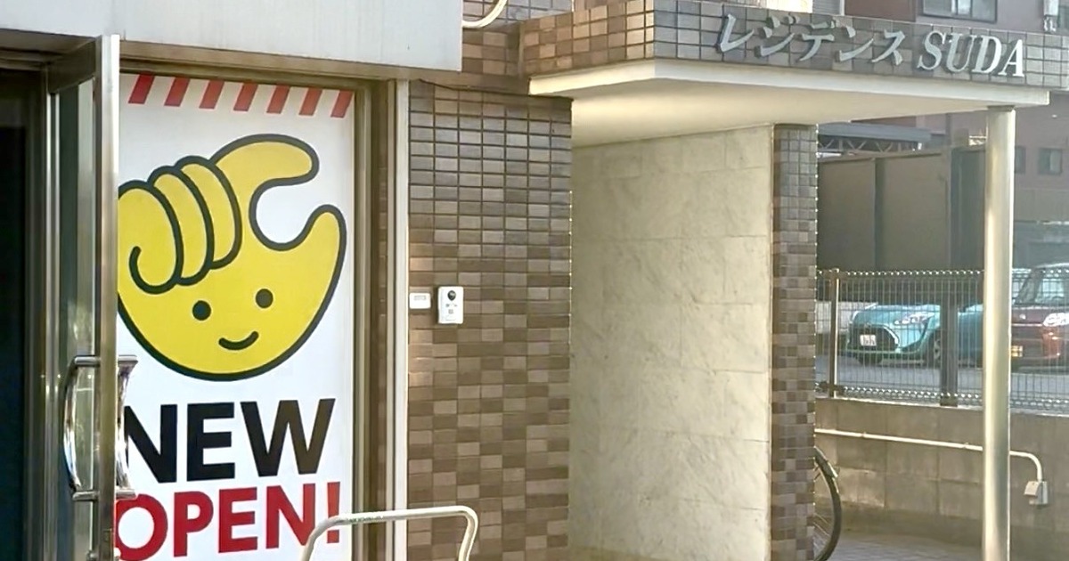八王子市松木のレジデンスSUDA1階入口。黄色い手のキャラクターとNEW OPEN!のチョコザップ開店告知が貼られ、右手のひさしにレジデンスSUDAの文字がある
