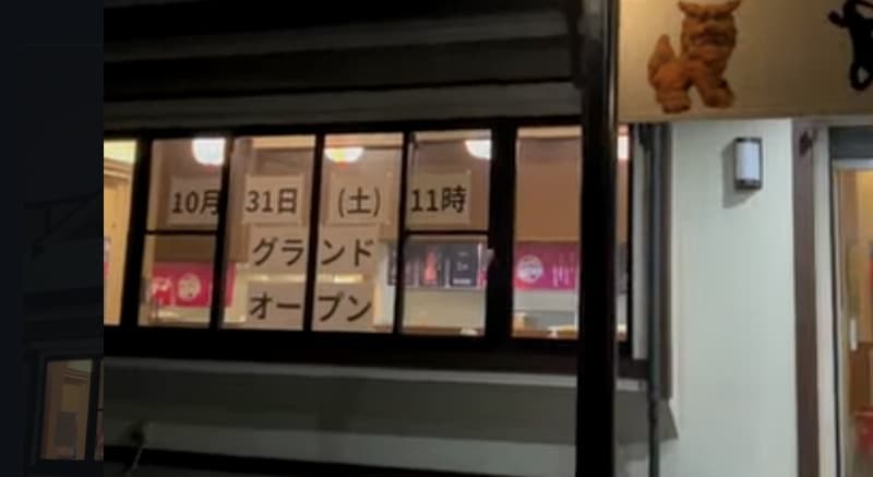 黒い窓枠の4枚窓に白い紙が貼られ、10月31日(土)11時、グランドオープンと書かれている。右端にシーサーが見える
